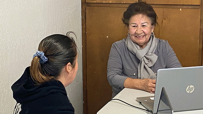 Photo of an older woman with a client at a desk with laptops